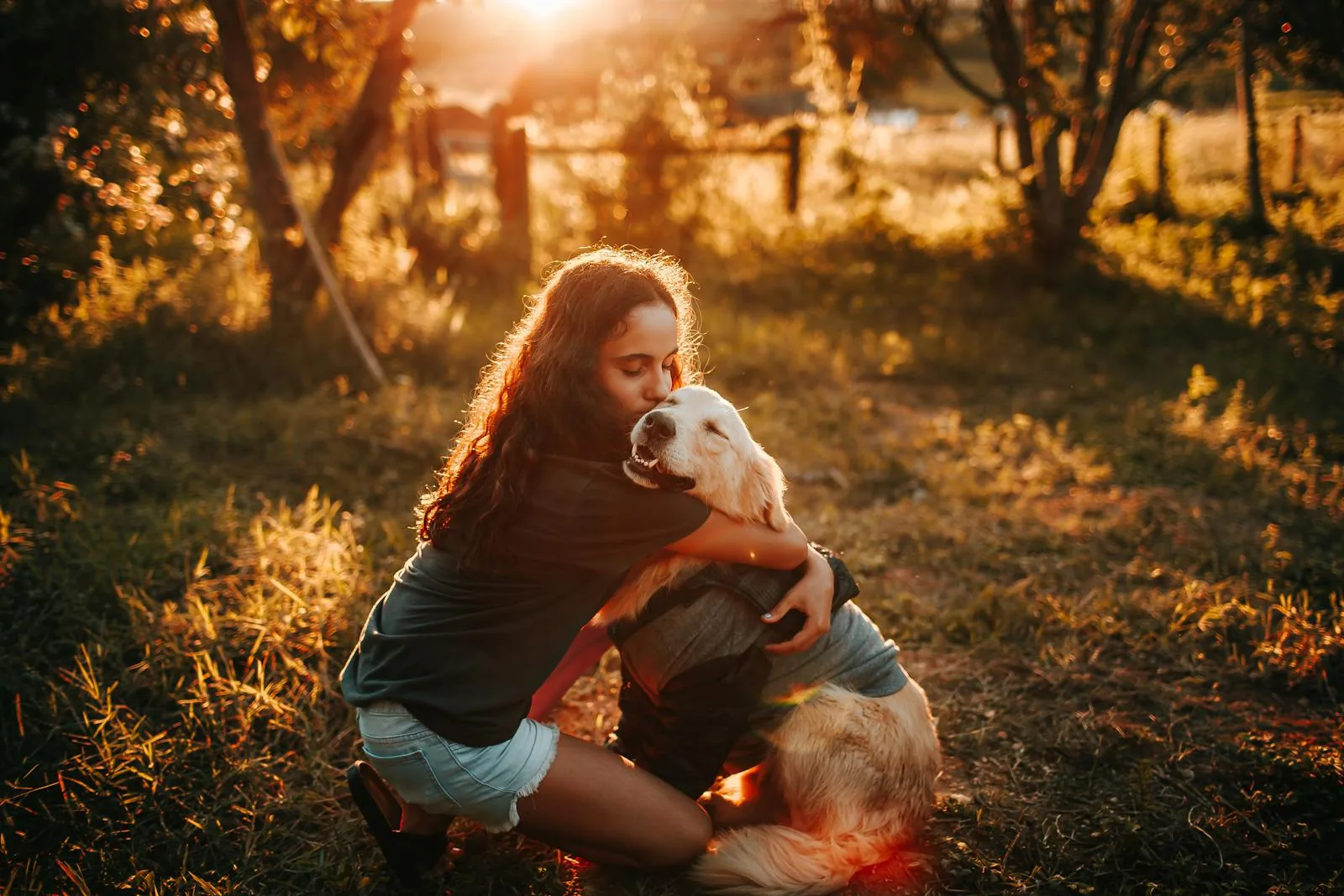 A woman hugs her Golden Retriever during a warm sunset in a grassy field &mdash; the same care, in the place you call home